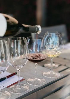 Pouring red wine into a glass on a table with multiple wine glasses and a notebook.