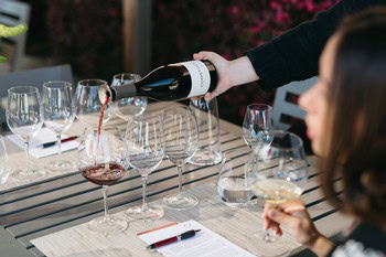 Person pouring red wine into glasses on a dining table for a wine tasting event.