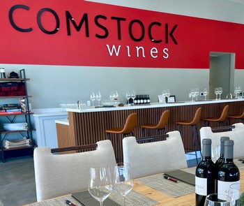 Modern wine tasting area with bar, wine bottles, glasses, and seating at Comstock Wines.