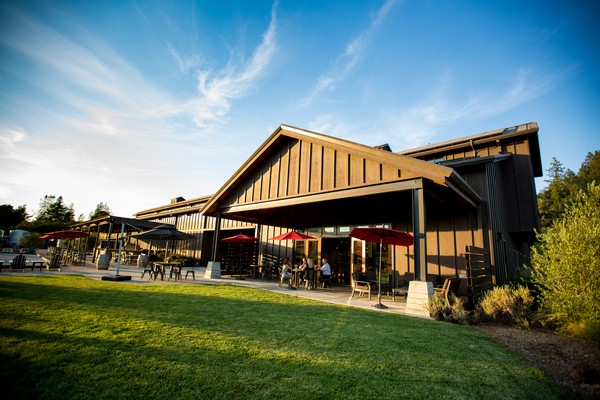 Contemporary restaurant with outdoor seating area, umbrellas, and lush green lawn under a blue sky.