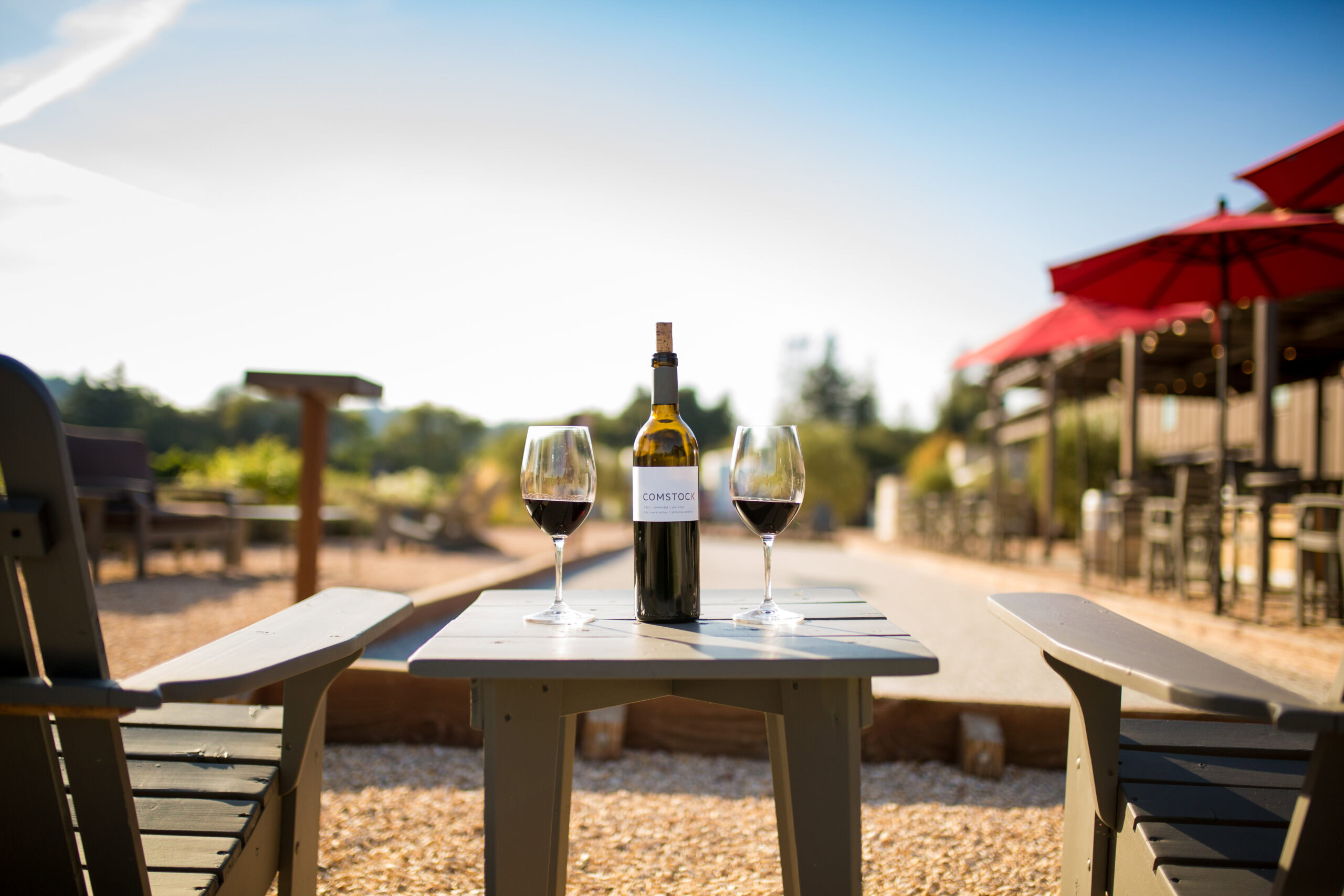Outdoor wine tasting setup with two glasses of red wine and a bottle on a table at Comstock Wines.