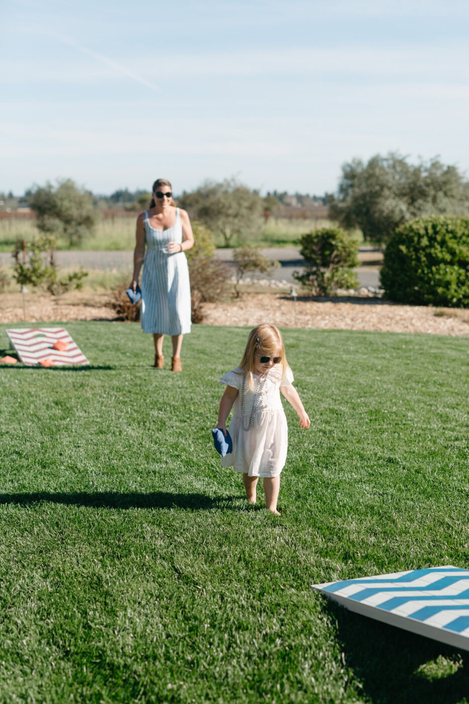 Woman and child walking on a grassy field with a picnic area in the background.