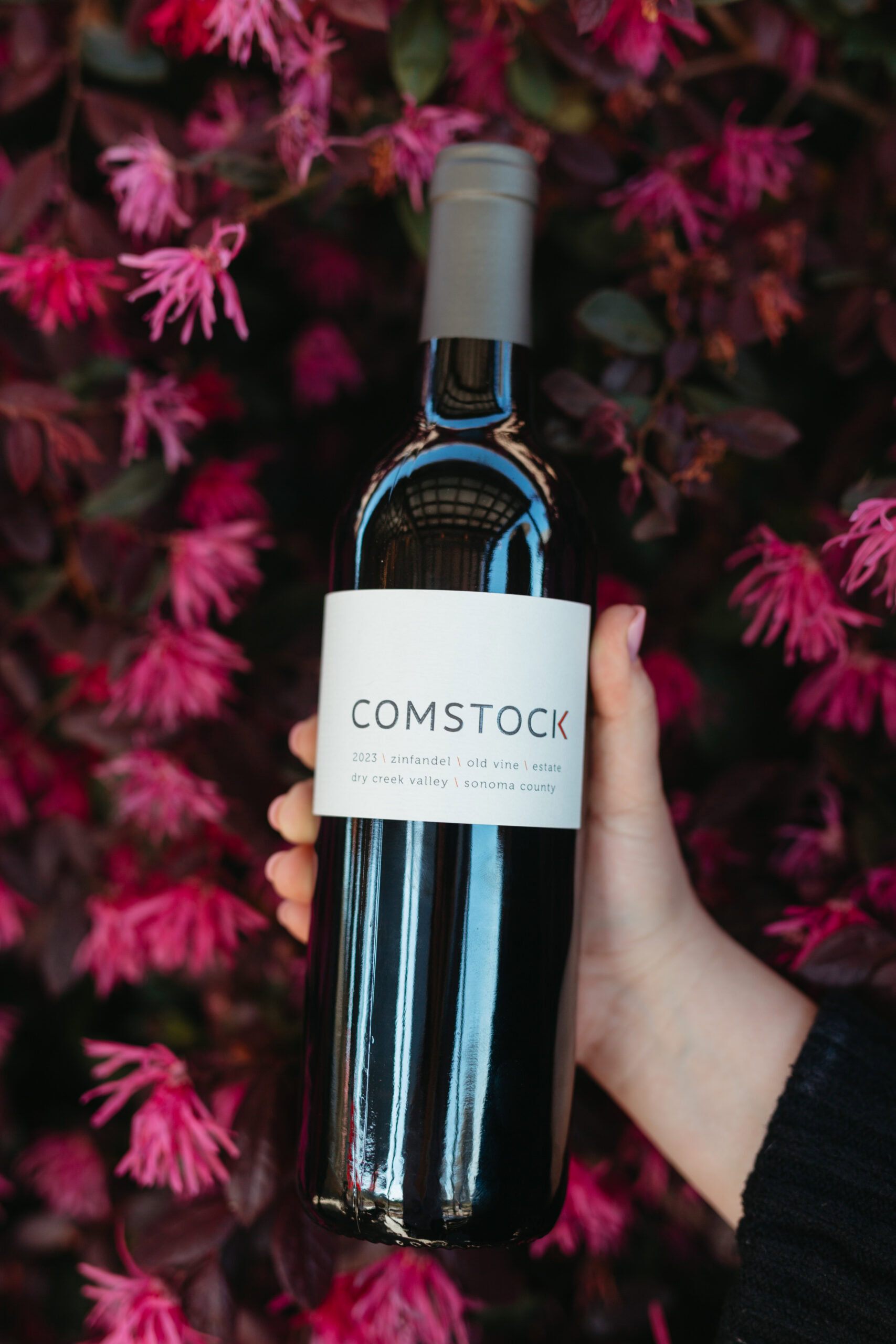 Elegant wine bottle from Comstock Wines held against vibrant pink flowers background.